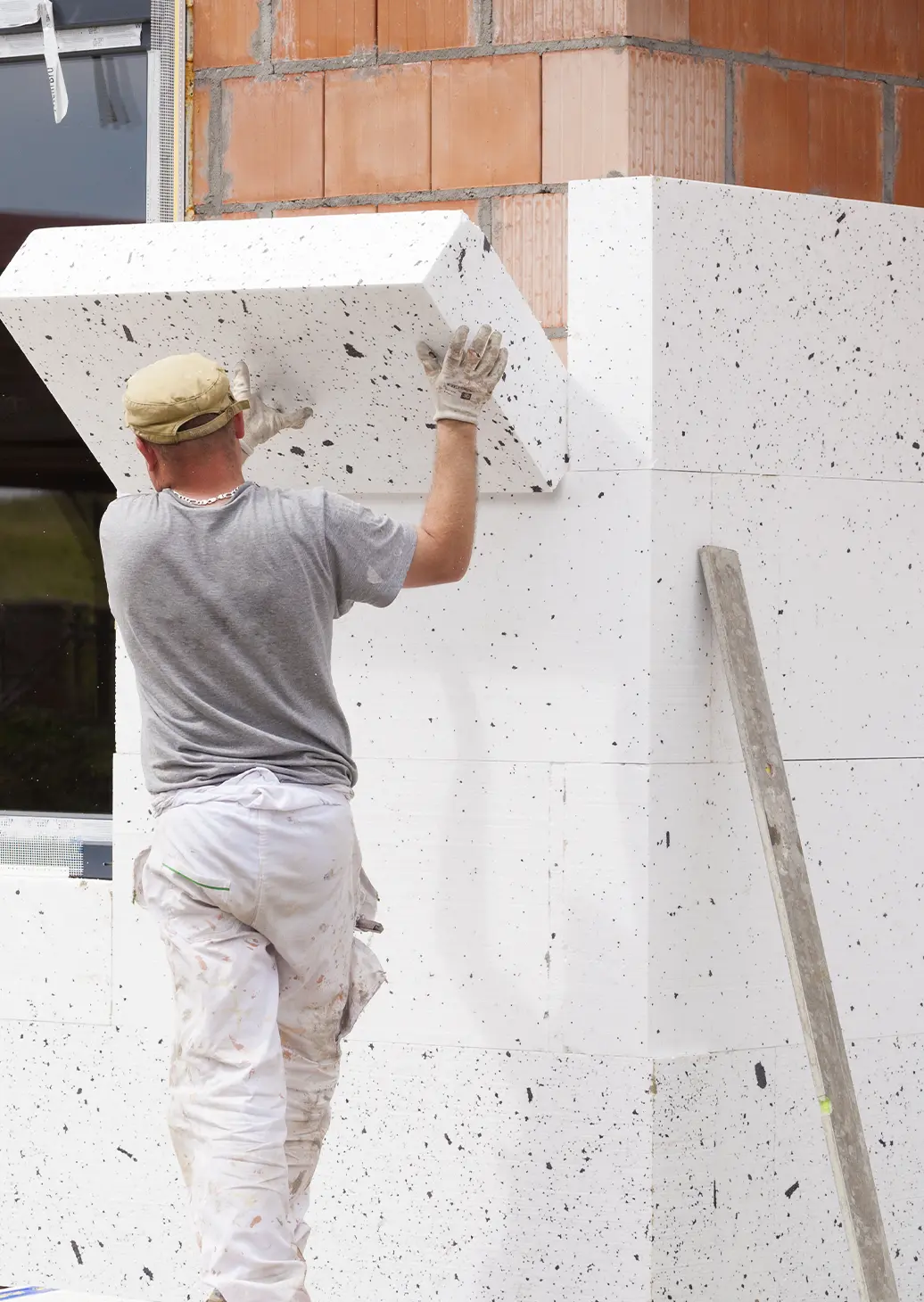 Artisan posant des panneaux isolants EPS sur mur extérieur — chantier ITE en Wallonie