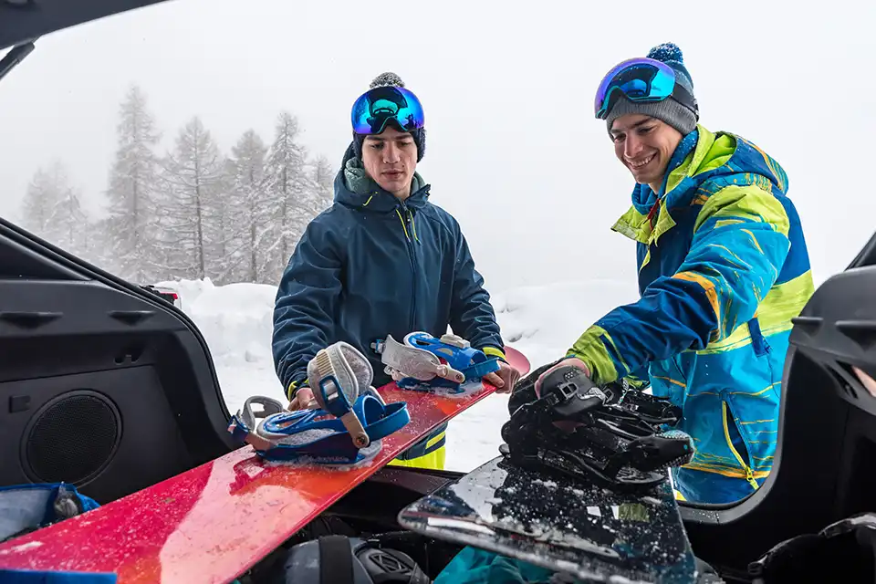 Deux snowboardeurs préparant leur matériel dans le coffre d'un véhicule alimenté par un panneau solaire flexible Kodak® en montagne enneigée