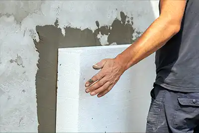 Pose d'un panneau de polystyrène ETICS contre un mur extérieur préparé en mortier gris en Wallonie