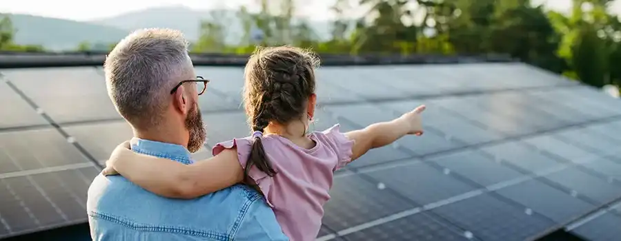 Père et sa fille contemplant les panneaux solaires photovoltaïques installés sur le toit de leur maison familiale en Belgique, avec un paysage verdoyant en arrière-plan
