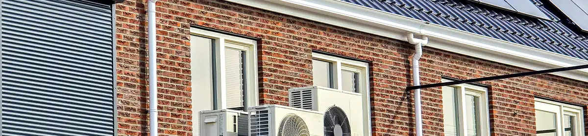 Trois unités extérieures de pompes à chaleur air-air installées sur une maison wallonne en briques rouges avec panneaux solaires en toiture