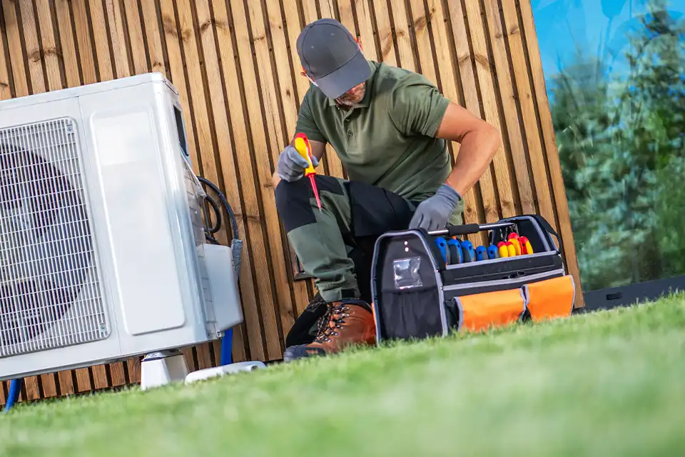 Technicien certifié installant une pompe à chaleur air-eau dans le jardin d'une maison résidentielle en Wallonie